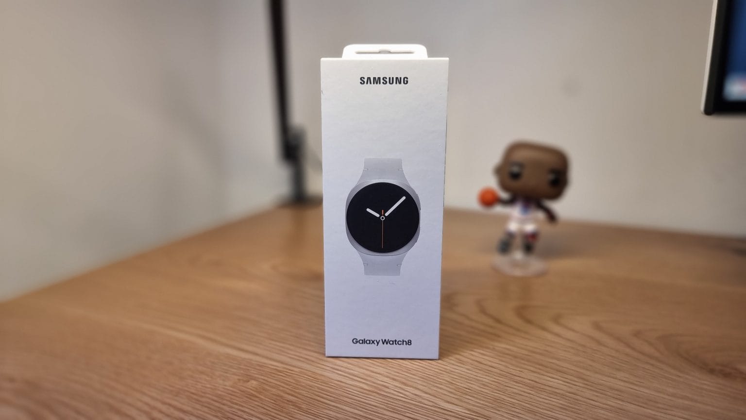 Samsung Galaxy Watch 8 - אריזת שעון חכם סמסונג גלקסי ווטש 8 בצבע לבן על שולחן עץ