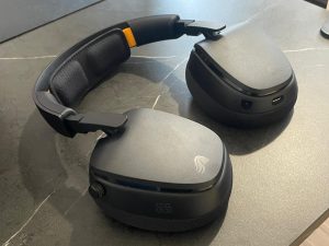 Glorious GHS Eternal RGB - אוזניות גיימינג בצבע שחור מונחות על משטח כהה, הכוללות ריפוד קשת, חוגת עוצמת שמע, חיבורים בתחתית האפרכסת וכיתוב GG WP.