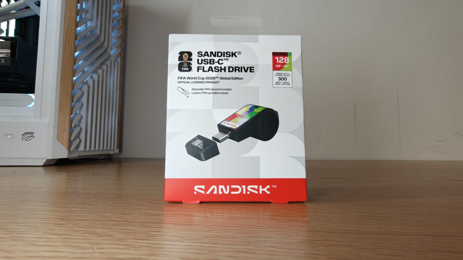 SANDISK Flash Drive FIFA 2026 - אריזת כונן נייד בחיבור USB-C בנפח 128GB מונחת על שולחן עץ