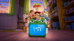 Toy Story 5 - וודי, ג'סי, באז שנות אור ושאר הצעצועים מביטים בטאבלט עם כיסוי צפרדע שעליו מופיע הכיתוב היי! בואו נשחק!