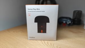 Kooduu Sensa Play Mini - קופסת האריזה של רמקול בלוטות' משולב תאורת לד מונחת על שולחן עץ