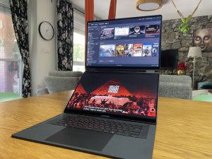 ROG Zephyrus Duo - מחשב נייד בעל מסך כפול פתוח על שולחן עץ ומציג את ספריית Steam וסרטון וידאו