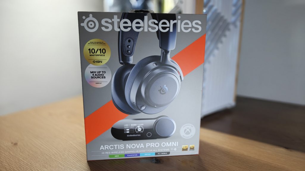 SteelSeries Arctis Nova Pro Omni - אריזת המוצר של האוזניות מונחת על שולחן עץ