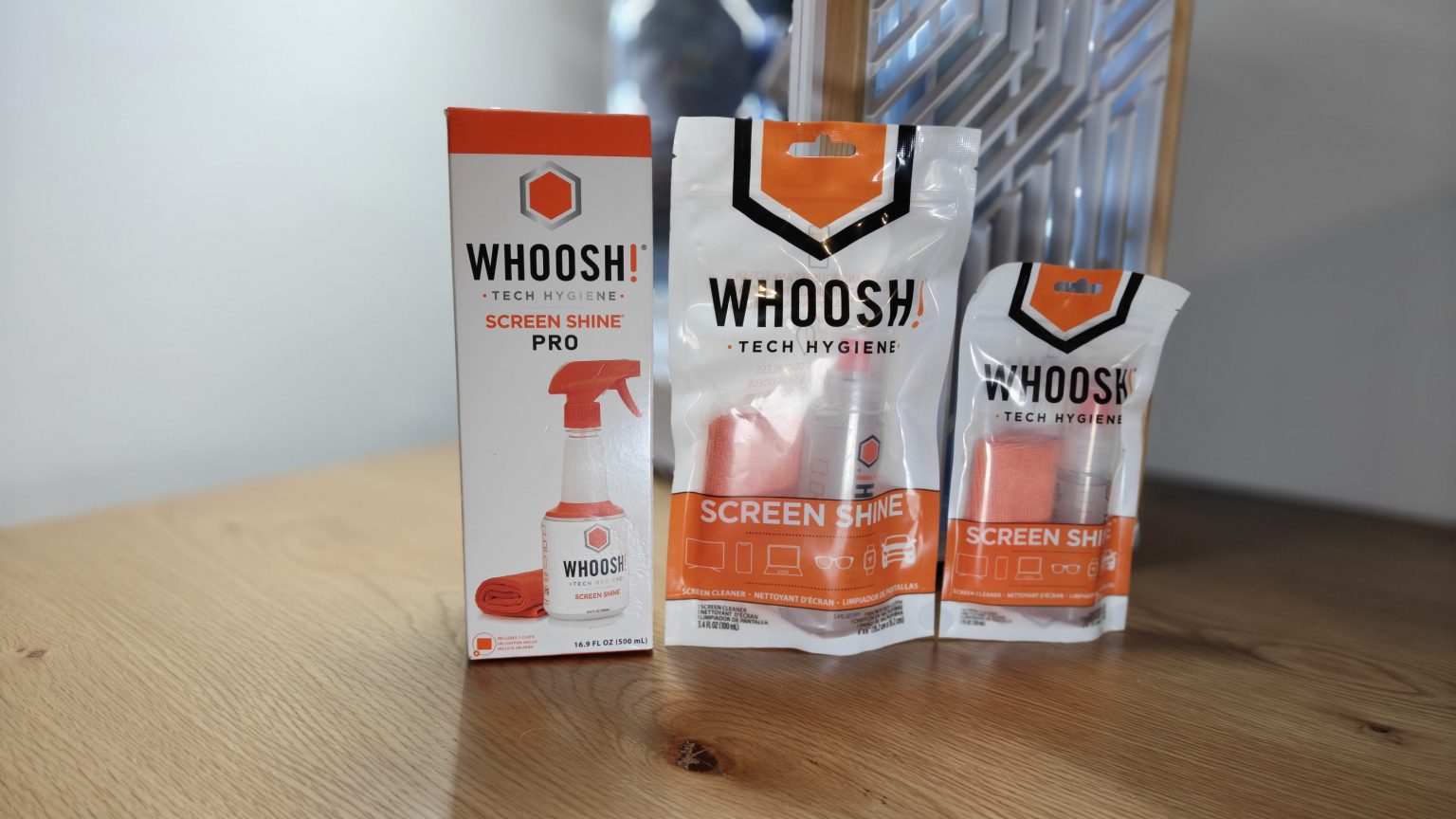 Whoosh Screen Shine - שלושה מארזים של תרסיסי ניקוי למסכים ומטליות מיקרופייבר בגדלים שונים על שולחן עץ