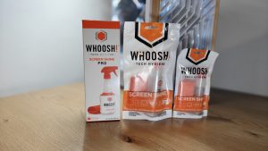Whoosh Screen Shine - שלושה מארזים של תרסיסי ניקוי למסכים ומטליות מיקרופייבר בגדלים שונים על שולחן עץ