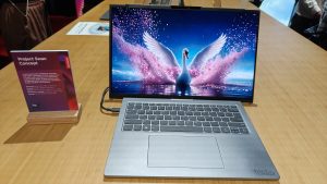 Lenovo Think -Project Swan מנגנון מסך נגלל ממונע פאנל תצוגה גמיש ורציף ללא צירים או מגרעות מנגנון מסך נגלל ממונע פאנל תצוגה גמיש ורציף ללא צירים או מגרעות - מחשב נייד קונספט מדגם ThinkBook פתוח על שולחן עץ עם תמונת ברבור על המסך ושלט מפרט לצידו
